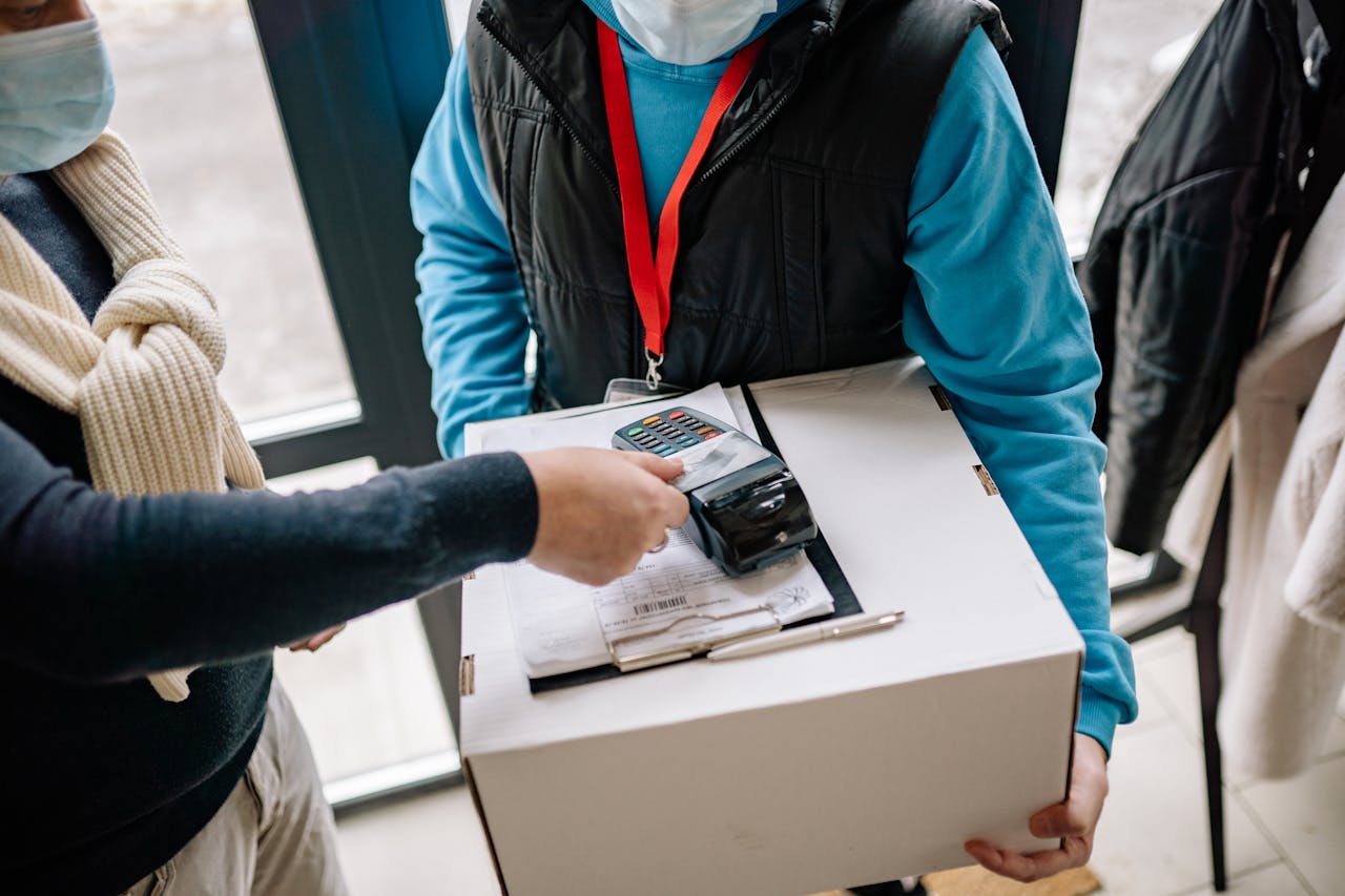 Masked customer uses contactless payment for package delivery indoors.
