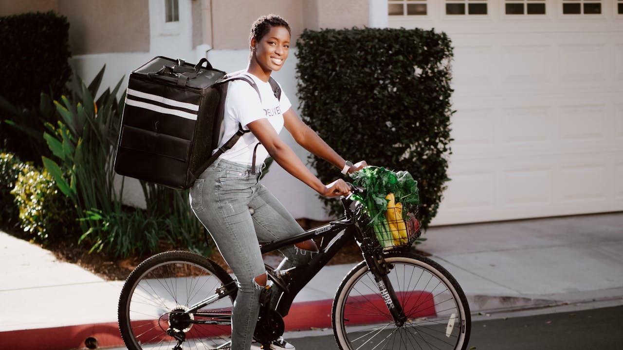 Smiling African American woman delivering goods on a bicycle with a delivery backpack.